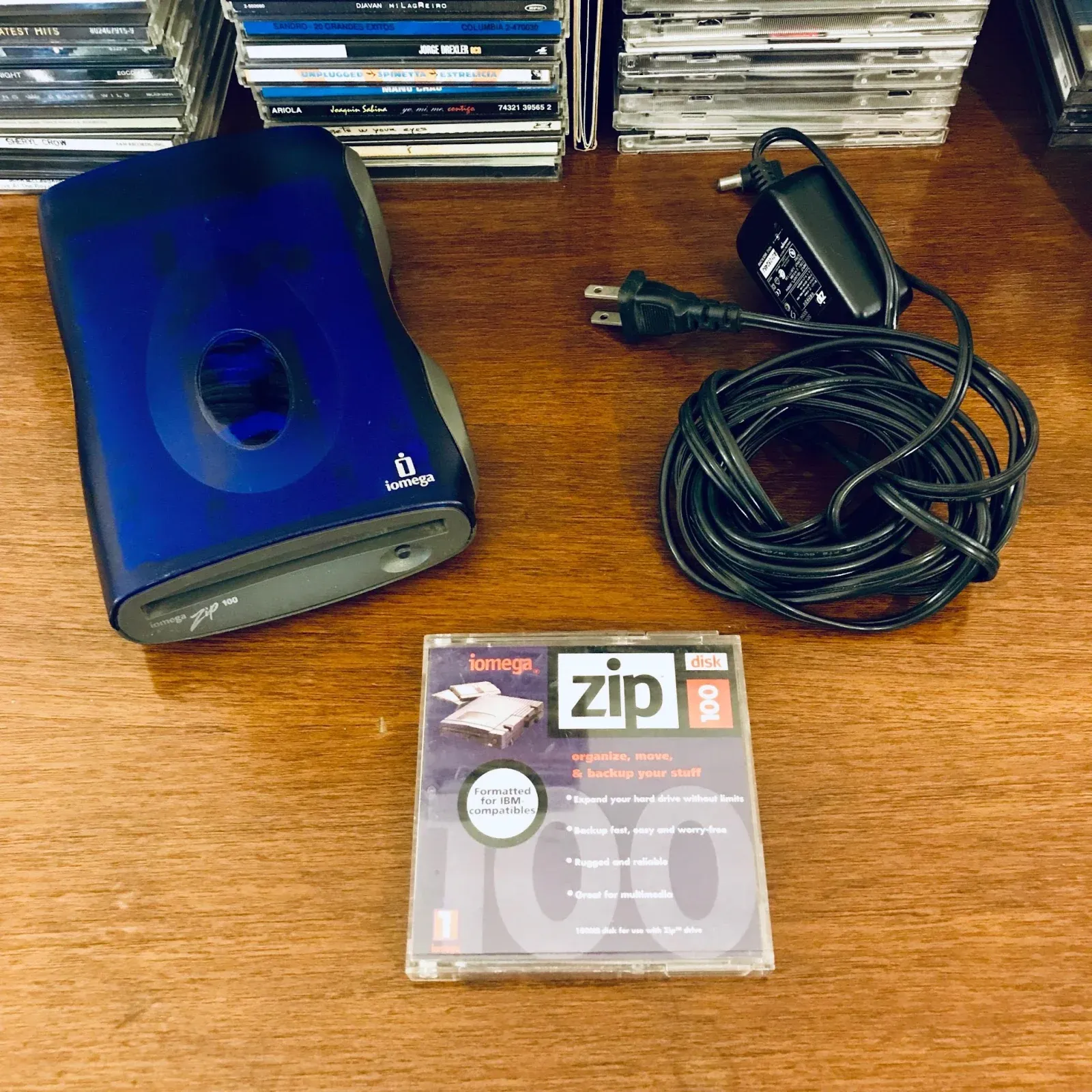 The actual blue Iomega Zip 100 drive on a desk with its power supply and a Zip disk.