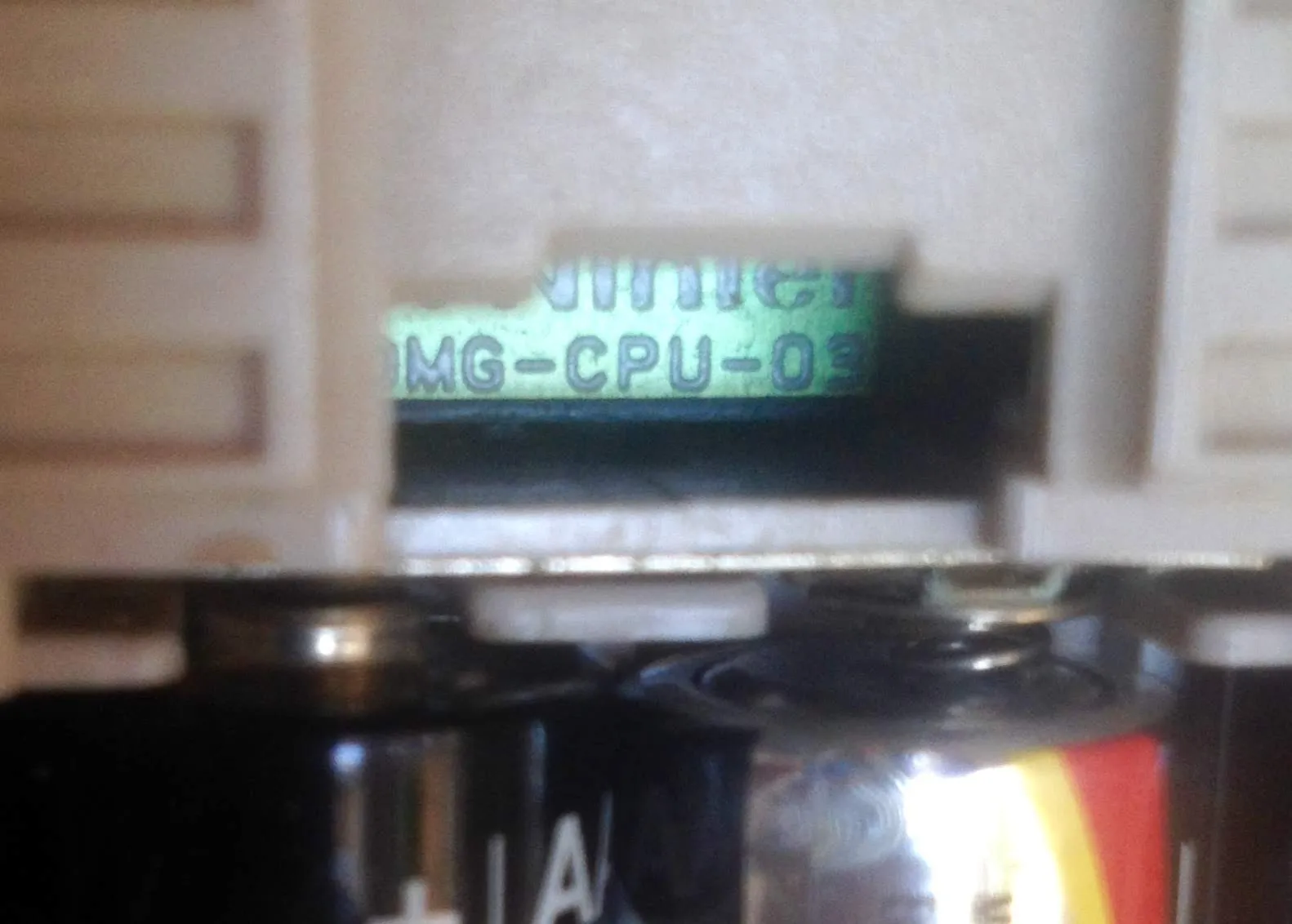 Close up through the battery compartment window of a Game Boy, showing a strip of green circuit board with DMG-CPU-03 printed on it in white silkscreen. Two AA batteries sit in the foreground.