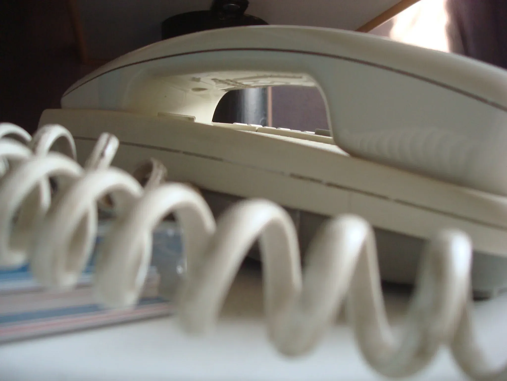 Close-up of a beige landline telephone receiver above its coiled cord.